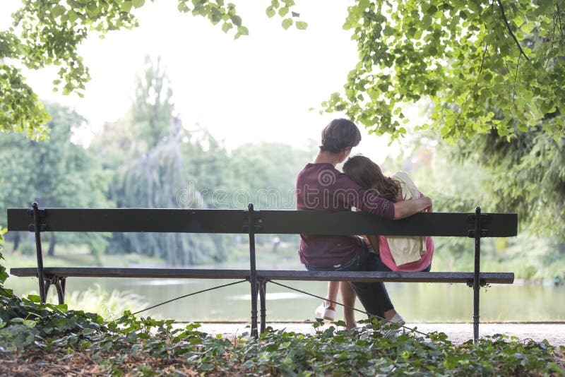 Hintere Ansicht von den romantischen jungen Paaren, die auf Bank am Seeufer sitzen