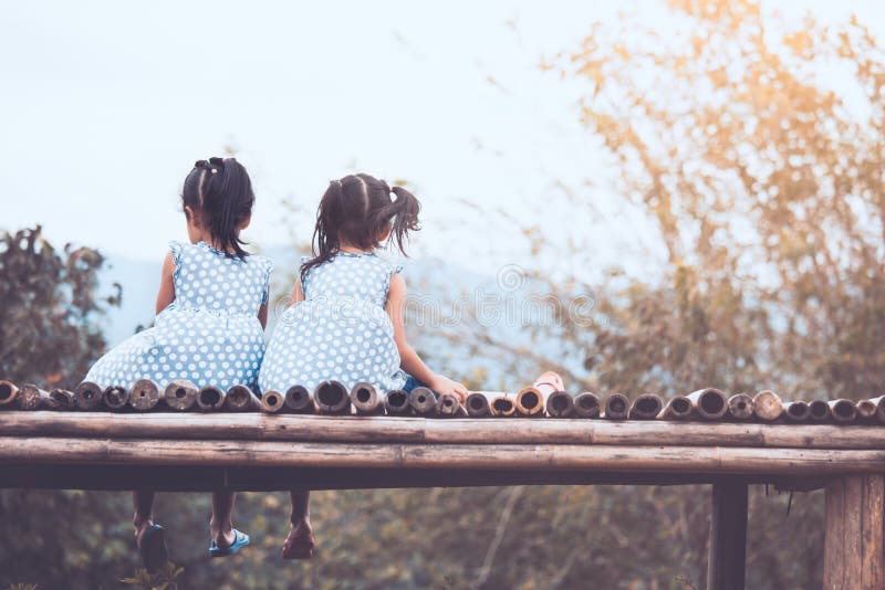 Hintere Ansicht von zwei Kindermädchen, die Natur sitzen und betrachten stockbild Hintere Ansicht von zwei Kindermädchen, die Natur sitzen und betrachten stockbild