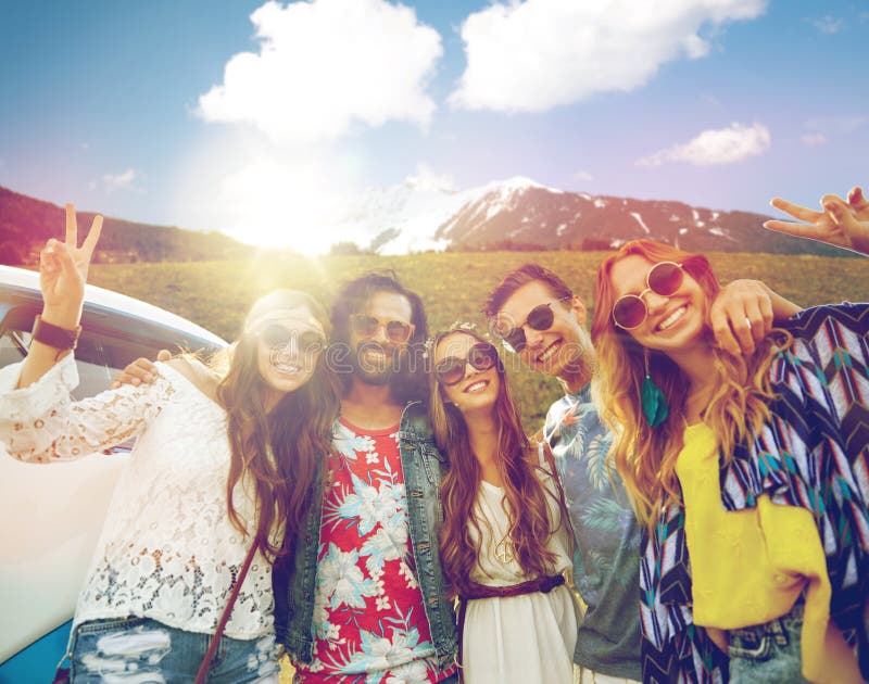 Summer holidays, road trip, travel and people concept - smiling young hippie friends at minivan car showing peace hand sign over alps mountains background. Summer holidays, road trip, travel and people concept - smiling young hippie friends at minivan car showing peace hand sign over alps mountains background