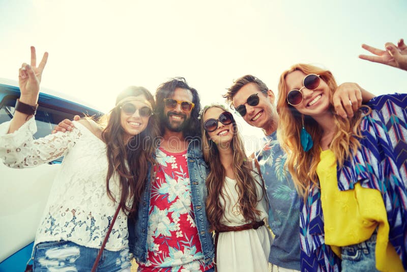 Summer holidays, road trip, vacation, travel and people concept - smiling young hippie friends over minivan car showing peace hand sign. Summer holidays, road trip, vacation, travel and people concept - smiling young hippie friends over minivan car showing peace hand sign