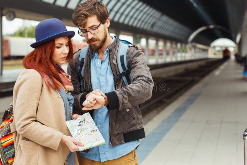 Hippie-Reisendpaare, die intelligente Uhr beim Warten auf den Zug am Bahnhof betrachten Autumn Time Frau stockbild Hippie-Reisendpaare, die intelligente Uhr beim Warten auf den Zug am Bahnhof betrachten Autumn Time Frau stockbild