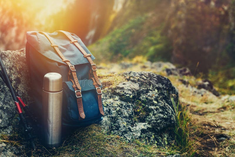 Hipster Blue Backpack, Thermos And Trekking Poles Closeup, Front View. Tourist Traveler Bag On Rocks Background. Adventure Hiking