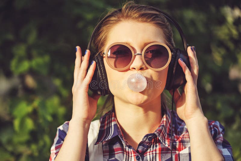 Hipster girl listening to music on headphones and chews the cud.