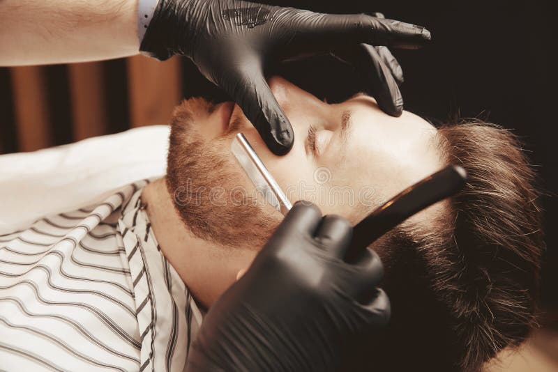 Hipster haircut makes beard in brutal barbershop with straight razor royalty free stock photography Hipster haircut makes beard in brutal barbershop with straight razor royalty free stock photography