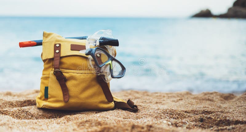 Hipster hiker tourist yellow backpack and swimming mask on background blue sea ocean horizon on sand beach, blurred panoramic seas