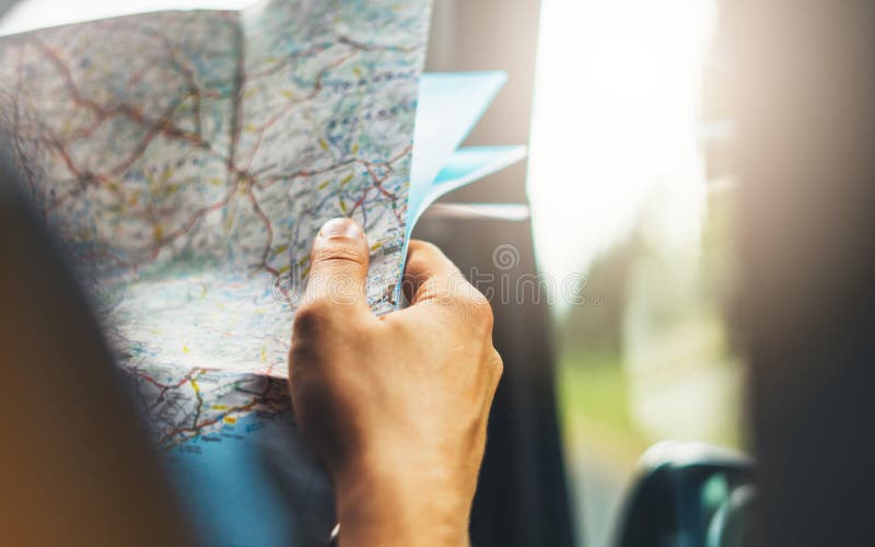 Hipster man holding in male hands and looking on navigation map in auto, tourist traveler hiker driving on background panoramic view way road, trip in transportation, person sitting on backdrop window auto