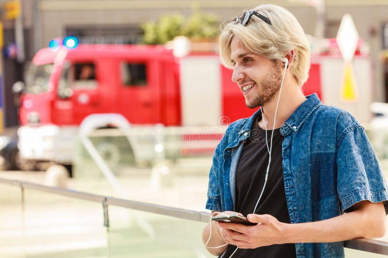 Hipster man standing on city street listening music