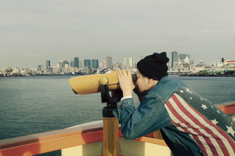 Hipster man wearing american flag jeans jacket looking through binocular lens against urban building royalty free stock photography Hipster man wearing american flag jeans jacket looking through binocular lens against urban building royalty free stock photography
