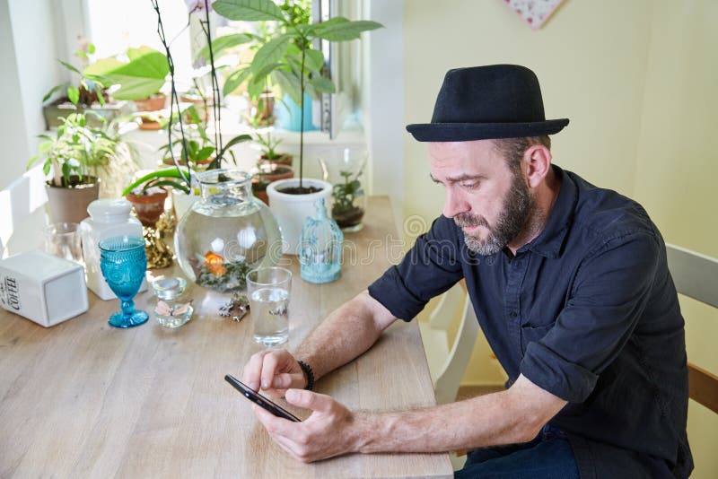 Hipster med skägget och hatt som ser iphone arkivfoton Hipster med skägget och hatt som ser iphone arkivfoton