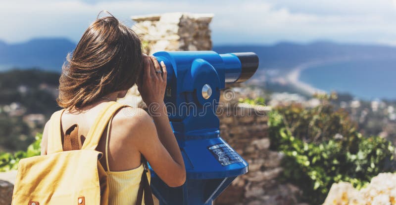 Hipster tourist look observant binoculars telescope on panoramic view, lifestyle concept trip, traveler with backpack on background mountain and blue sea landscape horizon, young girl hiker pointing hands