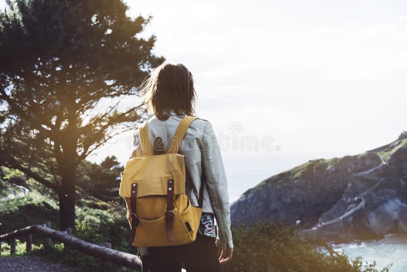 Hipster young girl with backpack enjoying sunset on seascape on peak mountain. Tourist traveler on background valley landscape