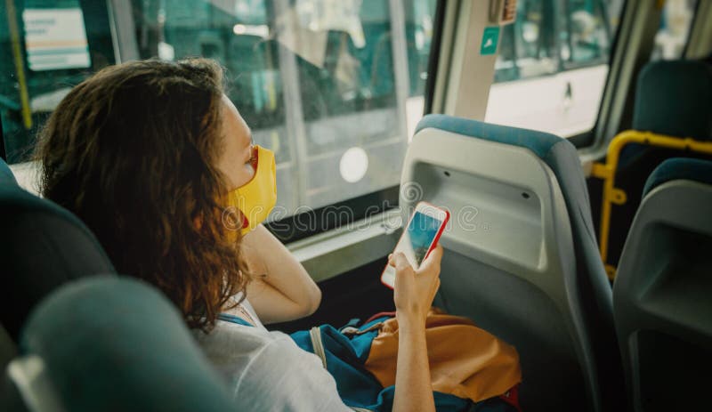 Hipster young girl in a protective mask on her face in a public transport bus with a smartphone in her hands stock photo Hipster young girl in a protective mask on her face in a public transport bus with a smartphone in her hands stock photo