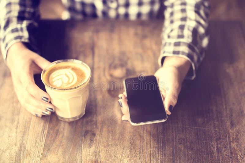 Hipstermeisje die een koffie en celtelefoon op houten lijst houden royalty-vrije stock fotografie Hipstermeisje die een koffie en celtelefoon op houten lijst houden royalty-vrije stock fotografie