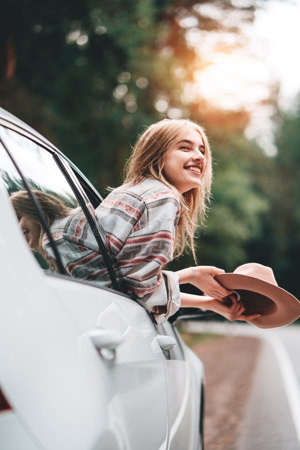 Hipstervrouw die door auto op wilde bosweg reizen Het knappe gelukkige meisje die geruite overhemd en hoed dragen zit bij het wie stock fotografie Hipstervrouw die door auto op wilde bosweg reizen Het knappe gelukkige meisje die geruite overhemd en hoed dragen zit bij het wie stock fotografie