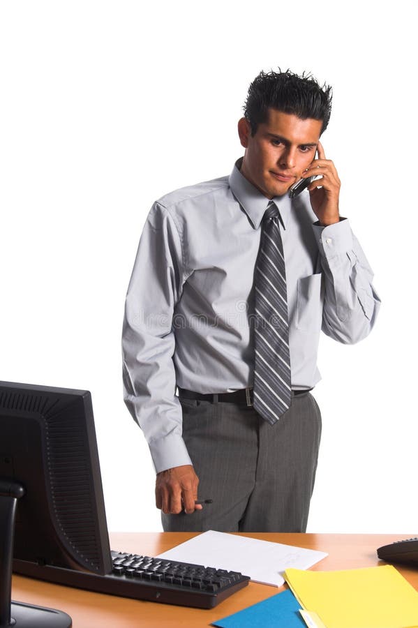 Handsome young Hispanic business man in a grey suit sans coat standing at his desk and taking a call on his cell phone with an unhappy expression on his face. Standing file folder stock images, royalty-free photos and pictures