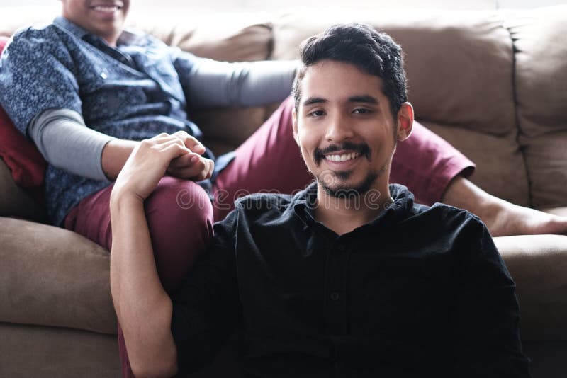 Homosexual couple, same sex marriage between hispanic men. Portrait of male partners and friends holding hands on sofa at home. Homosexual couple, same sex marriage between hispanic men. Portrait of male partners and friends holding hands on sofa at home.