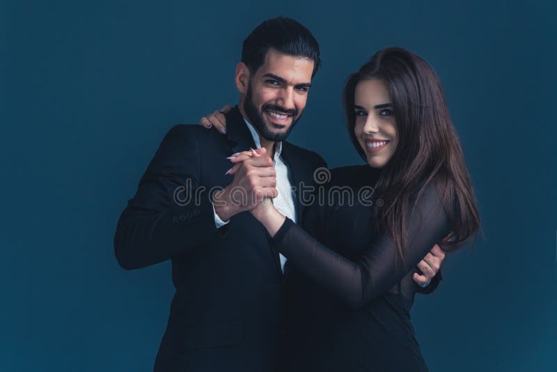 Hispanic man with beard dressed in suit slow dancing with dark-haired woman in black clothes. Young couple. Dark