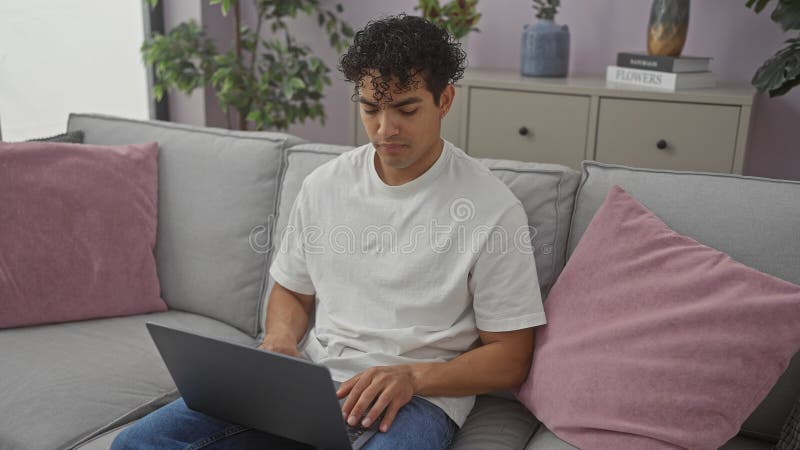 Hispanic man using laptop on couch in a modern living room setting royalty free stock photos