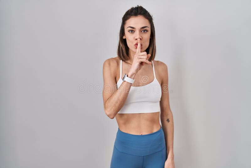 Hispanic woman wearing sportswear over isolated background asking to be quiet with finger on lips