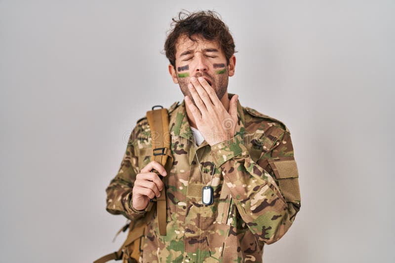 Hispanic young man wearing camouflage army uniform bored yawning tired covering mouth with hand