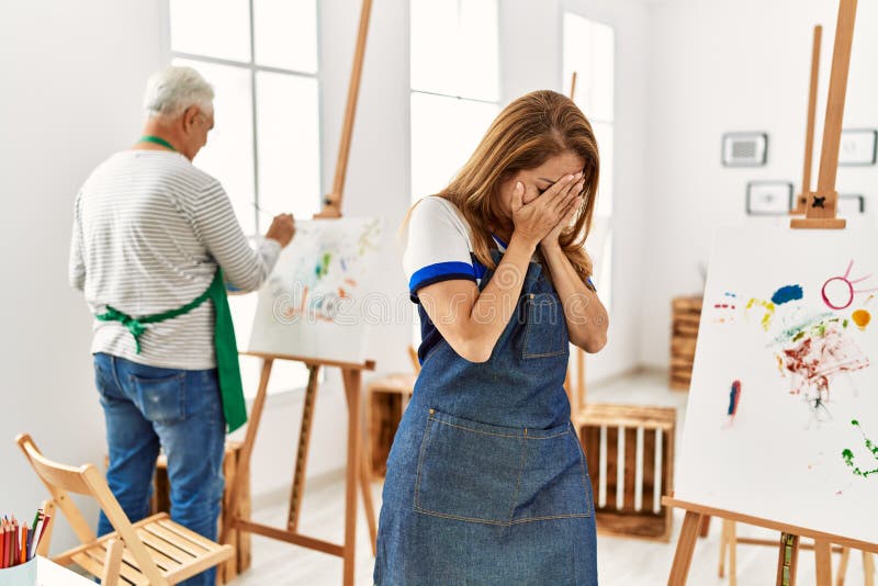 Hispanic woman wearing apron at art studio with sad expression covering face with hands while crying. depression concept. Hispanic woman wearing apron at art studio with sad expression covering face with hands while crying. depression concept