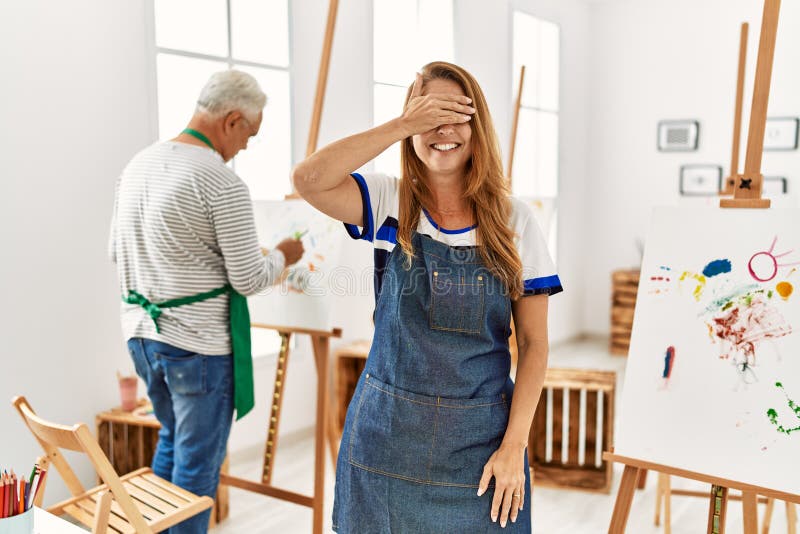 Hispanic woman wearing apron at art studio smiling and laughing with hand on face covering eyes for surprise. blind concept. Hispanic woman wearing apron at art studio smiling and laughing with hand on face covering eyes for surprise. blind concept