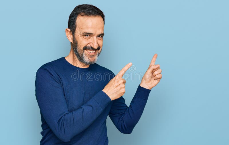 Hispano de mediana edad con ropa casual sonriendo y mirando la cámara apuntando con dos manos y dedos hacia un lado foto de archivo