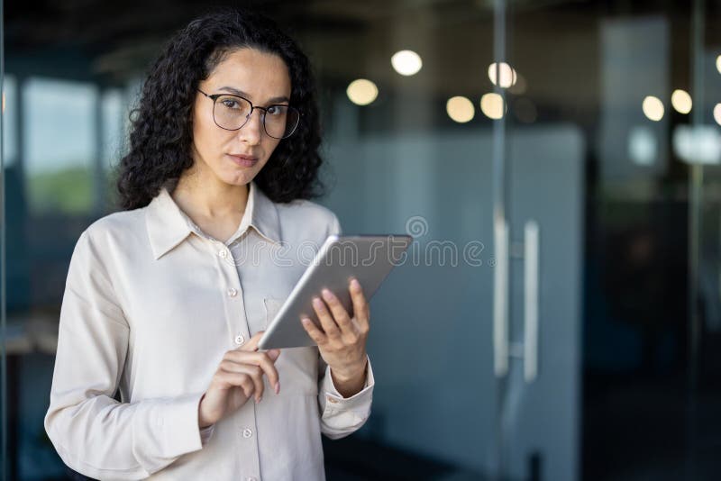 A focused Hispanic business woman in a light blouse uses a digital tablet in an office environment, possibly reviewing data or managing tasks. A focused Hispanic business woman in a light blouse uses a digital tablet in an office environment, possibly reviewing data or managing tasks.
