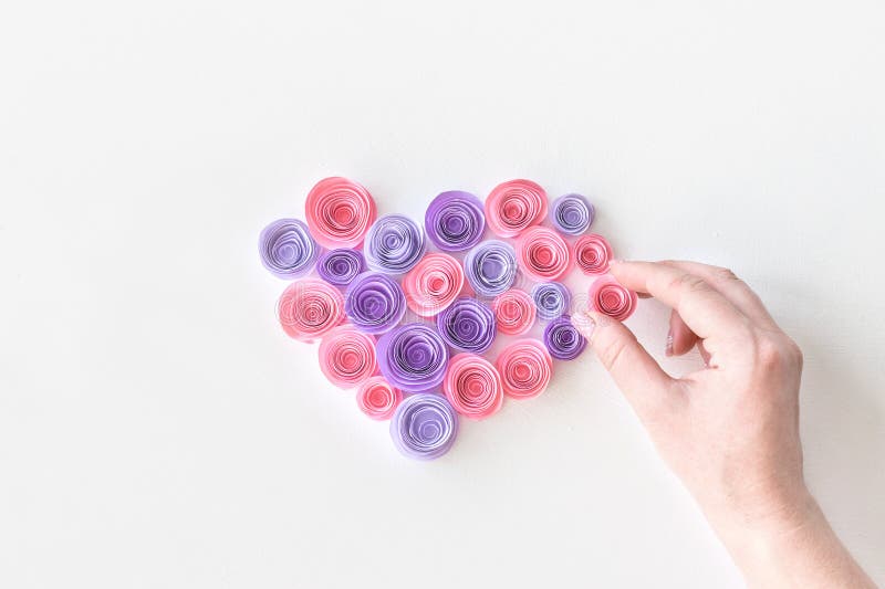 Hjärta som göras av pappers- rosa färg- och lilablommor med handen för kvinna` s Den kvinnliga handen sätter en blomma i hjärtafo royaltyfria bilder Hjärta som göras av pappers- rosa färg- och lilablommor med handen för kvinna` s Den kvinnliga handen sätter en blomma i hjärtafo royaltyfria bilder