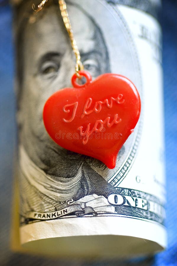 A red heart with I love you embossed on it tied with a gold string around a one hundred dollar bill. A red heart with I love you embossed on it tied with a gold string around a one hundred dollar bill.