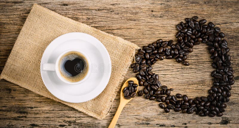 Hjärtekaffe och kaffebönor rostade i säck på ett golv av trä royaltyfri foto