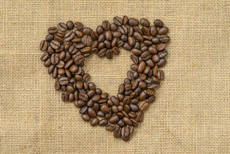 Hjärtkaffe Rostade kaffebönor i form av hjärta på naturlig duk, sagduk Begreppet 'kaffekärlek' eller 'älskad' arkivfoto