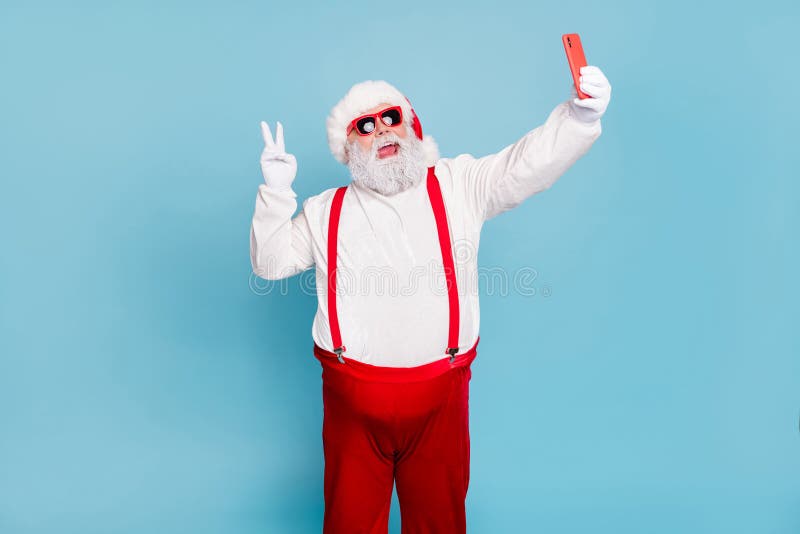 Ho-ho-ho. Portrait of overweight style funny hipster santa claus blogger in cap hat take selfie on cellphone make v royalty free stock photography Ho-ho-ho. Portrait of overweight style funny hipster santa claus blogger in cap hat take selfie on cellphone make v royalty free stock photography