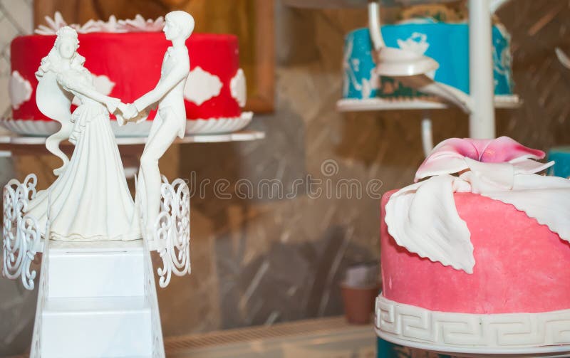 Wedding figurines placed on the scale of love and three wedding cakes : blue red and pink decorated with sugar flowers. Wedding figurines placed on the scale of love and three wedding cakes : blue red and pink decorated with sugar flowers.