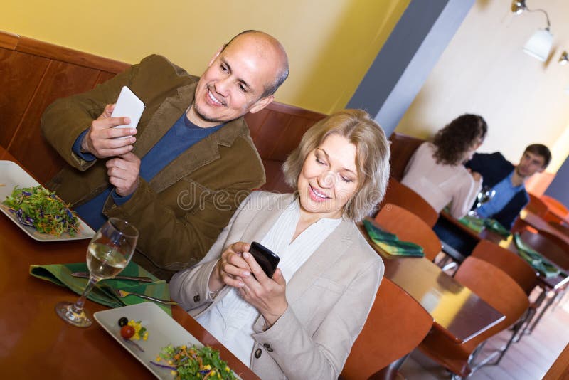 Hoger paar bezig met telefoons op datum in koffie stock foto's Hoger paar bezig met telefoons op datum in koffie stock foto's