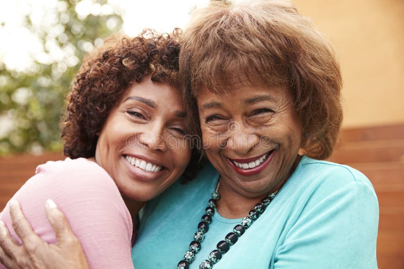 Hogere Afrikaanse Amerikaanse mum en haar midden oude dochterglimlach die aan camera, sluiten omhoog omhelzen