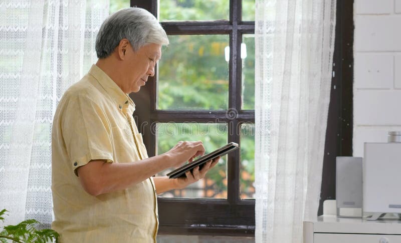 Hogere aziatische man die digitale tabletcomputer gebruikt op de thuisachtergrond, Oudere aziatische man en digitale tablet staat royalty-vrije stock foto Hogere aziatische man die digitale tabletcomputer gebruikt op de thuisachtergrond, Oudere aziatische man en digitale tablet staat royalty-vrije stock foto