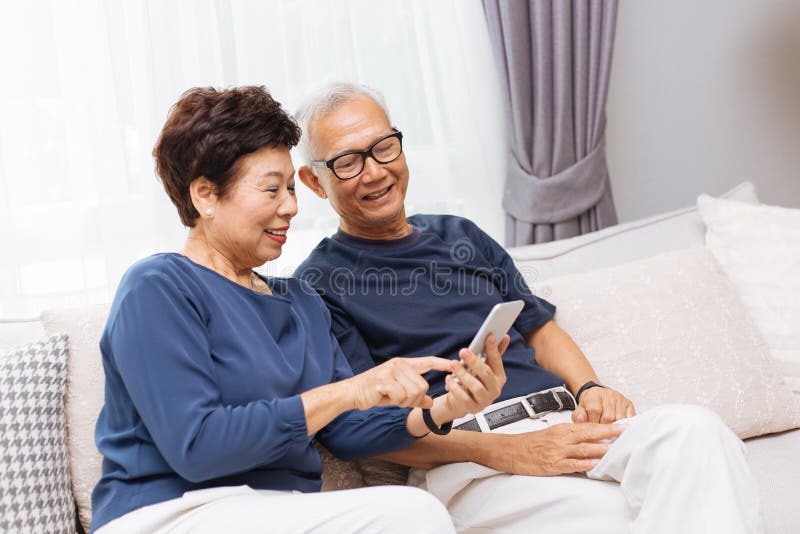 Hogere Aziatische paargrootouders die een slimme telefoon samen op bank met behulp van thuis royalty-vrije stock foto Hogere Aziatische paargrootouders die een slimme telefoon samen op bank met behulp van thuis royalty-vrije stock foto