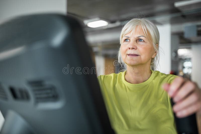 Hogere dame die op tredestepper bij gymnastiek uitoefenen stock foto's Hogere dame die op tredestepper bij gymnastiek uitoefenen stock foto's