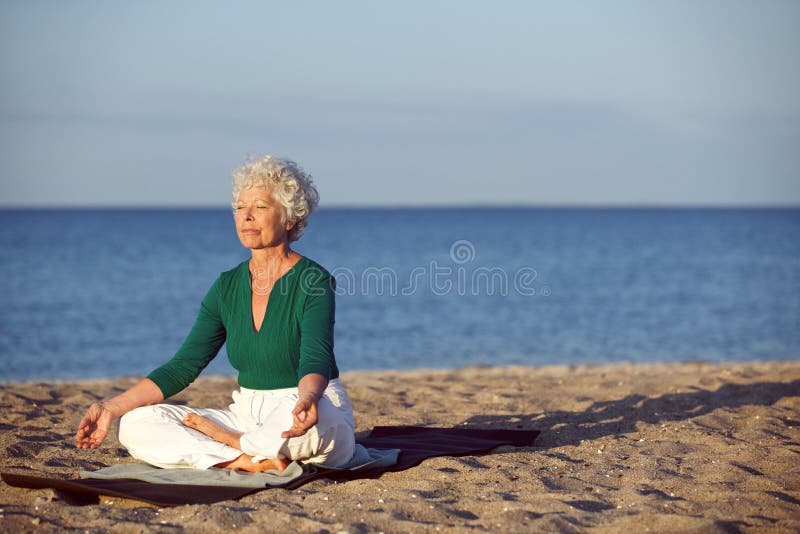 Hogere Kaukasische vrouw die op het strand mediteren