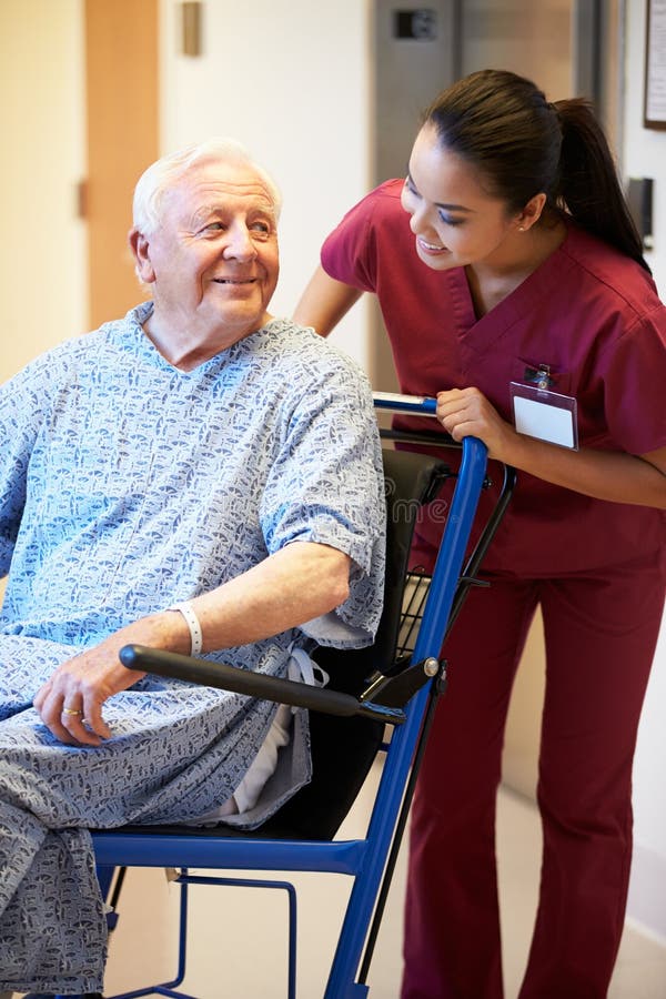 Senior Male Patient Being Pushed In Wheelchair By Nurse Looking At Each Other Smiling. Senior Male Patient Being Pushed In Wheelchair By Nurse Looking At Each Other Smiling