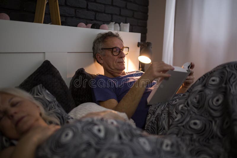 Hogere mens die in het boek van de bedlezing liggen royalty-vrije stock fotografie Hogere mens die in het boek van de bedlezing liggen royalty-vrije stock fotografie