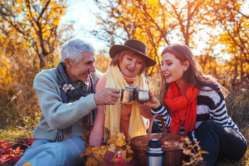 Hogere ouders die thee in de herfstbos drinken met hun dochter Familiewaarden Het hebben van picknick royalty-vrije stock foto's Hogere ouders die thee in de herfstbos drinken met hun dochter Familiewaarden Het hebben van picknick royalty-vrije stock foto's