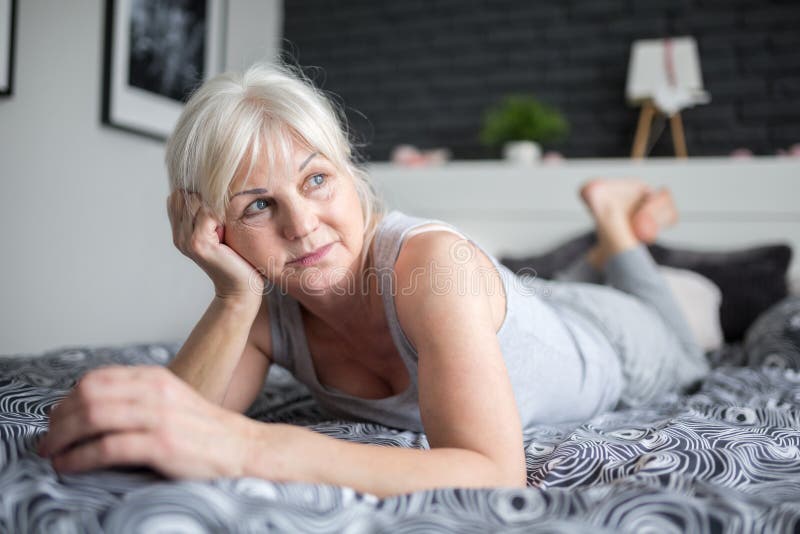 Hogere peinzende dame die op bed liggen die weg eruit zien royalty-vrije stock afbeelding Hogere peinzende dame die op bed liggen die weg eruit zien royalty-vrije stock afbeelding