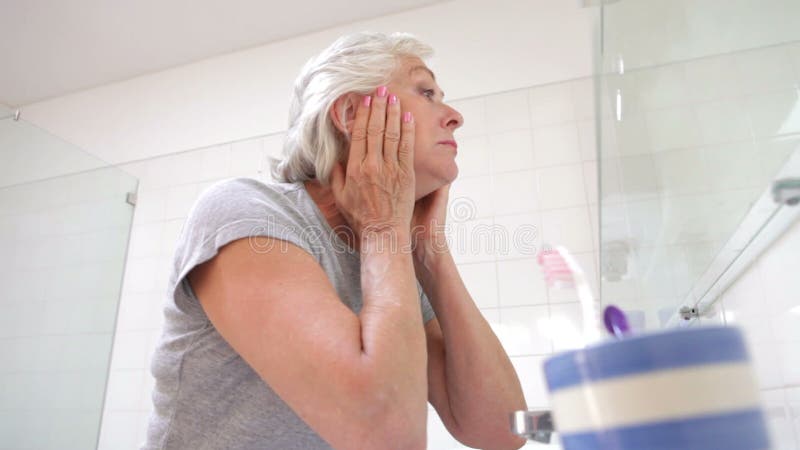 Hogere Vrouw die Huid in Badkamersspiegel controleren