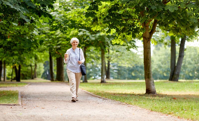 Hogere vrouw die met meeneemkoffie bij park lopen stock foto Hogere vrouw die met meeneemkoffie bij park lopen stock foto