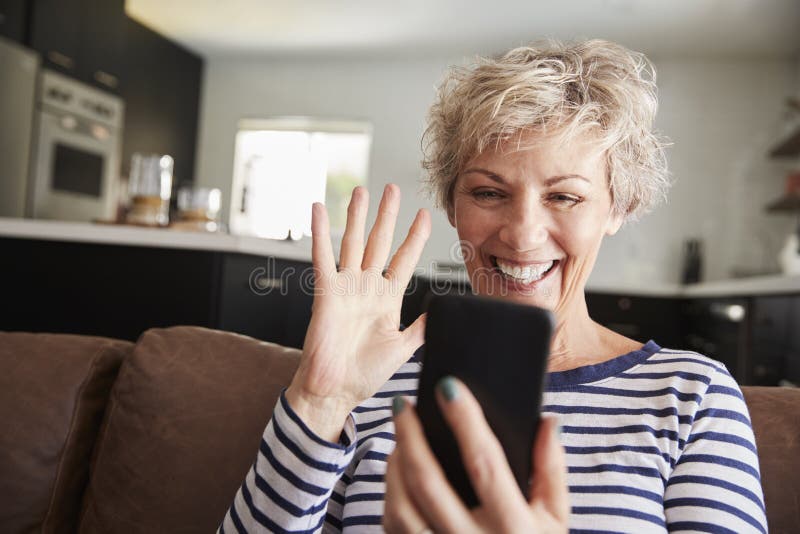 Hogere vrouw video het uitnodigen smartphone thuis, sluit omhoog stock afbeelding Hogere vrouw video het uitnodigen smartphone thuis, sluit omhoog stock afbeelding
