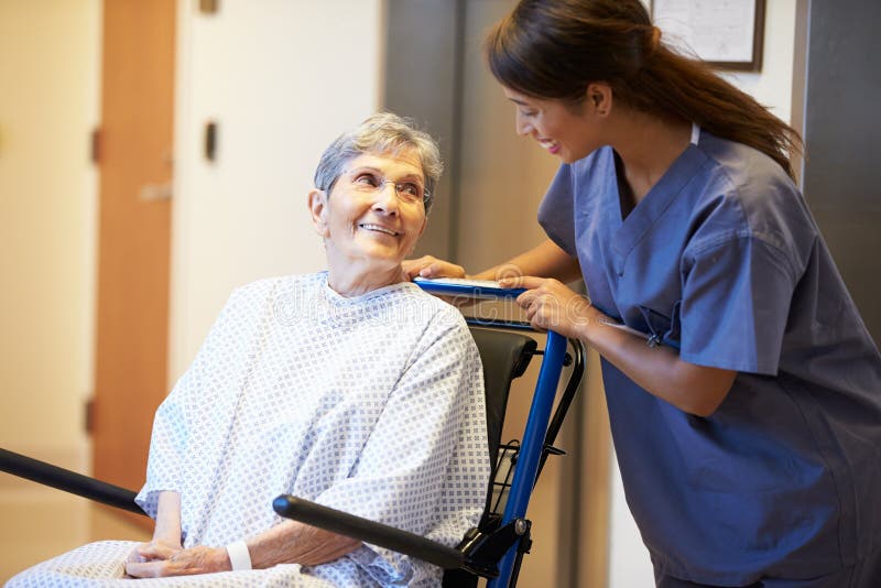 Senior Female Patient Being Pushed In Wheelchair By Nurse In Hospital Smiling. Senior Female Patient Being Pushed In Wheelchair By Nurse In Hospital Smiling