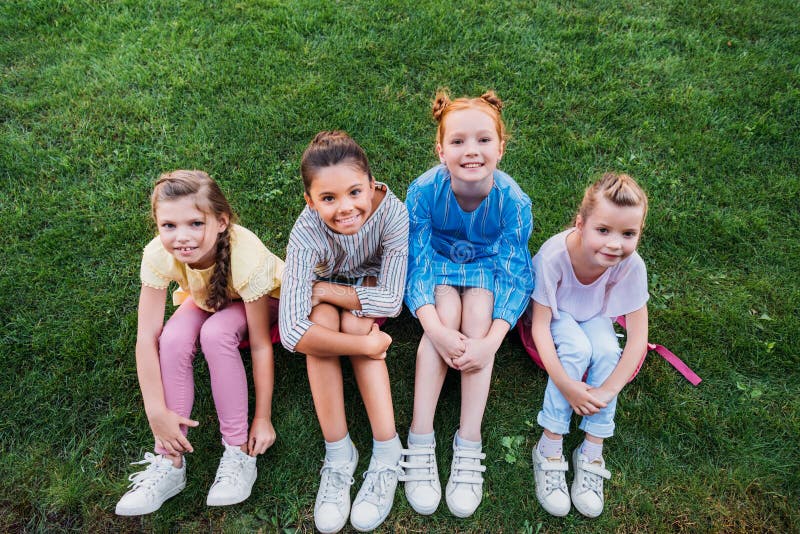 hohe Winkelsicht der Gruppe glücklicher Schulmädchen, die zusammen auf grünem Gras sitzen und Kamera betrachten lizenzfreie stockfotos hohe Winkelsicht der Gruppe glücklicher Schulmädchen, die zusammen auf grünem Gras sitzen und Kamera betrachten lizenzfreie stockfotos