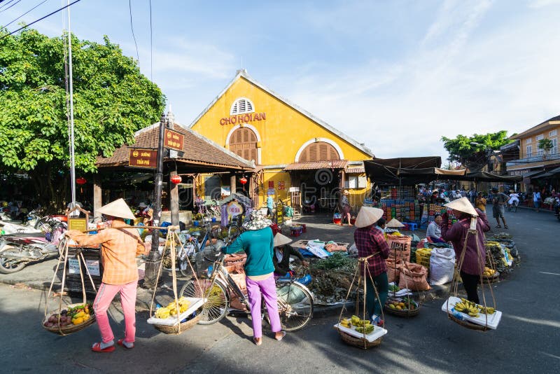 Hoi An, Vietnam - June 2019: street fruit vendors walking by colorful market building in old town stock images Hoi An, Vietnam - June 2019: street fruit vendors walking by colorful market building in old town stock images